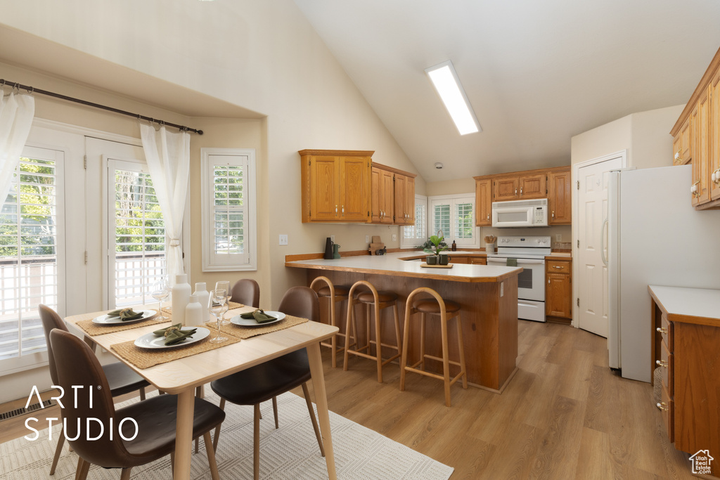 Kitchen with white appliances, a peninsula, high vaulted ceiling, light countertops, and light wood-type flooring