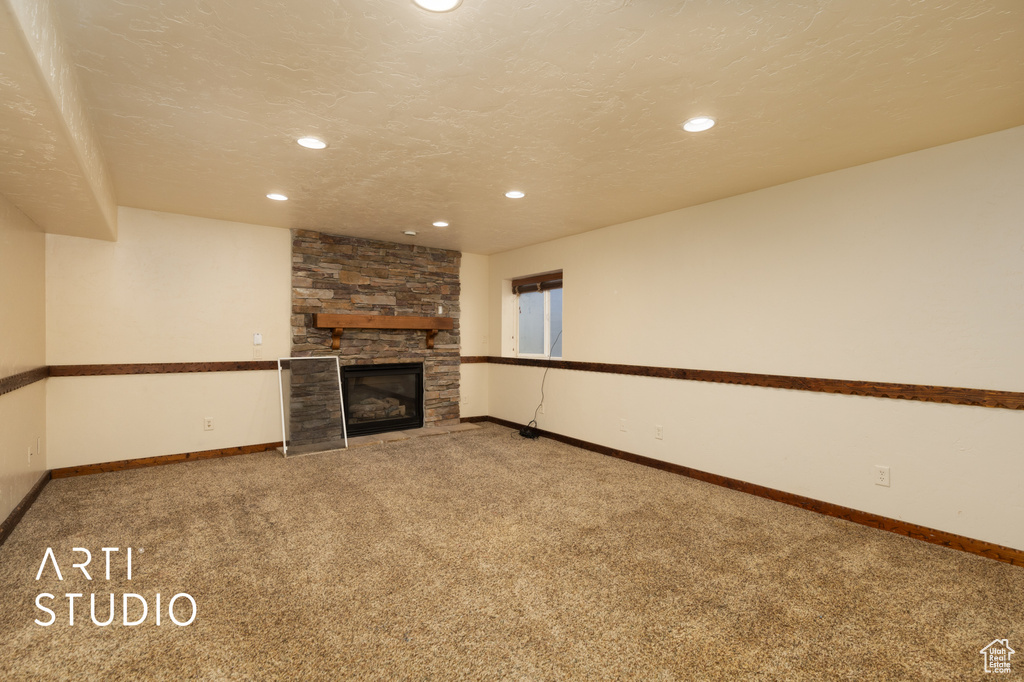 Unfurnished living room with carpet, a stone fireplace, and recessed lighting