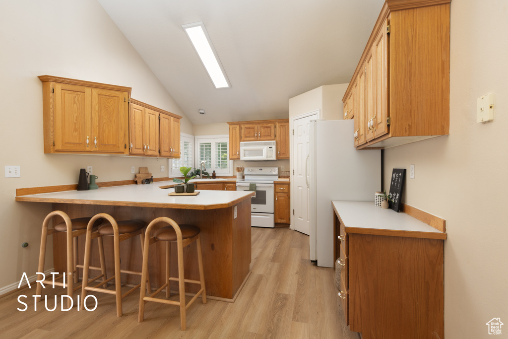 Kitchen featuring a peninsula, light wood-style floors, a breakfast bar area, white appliances, and high vaulted ceiling