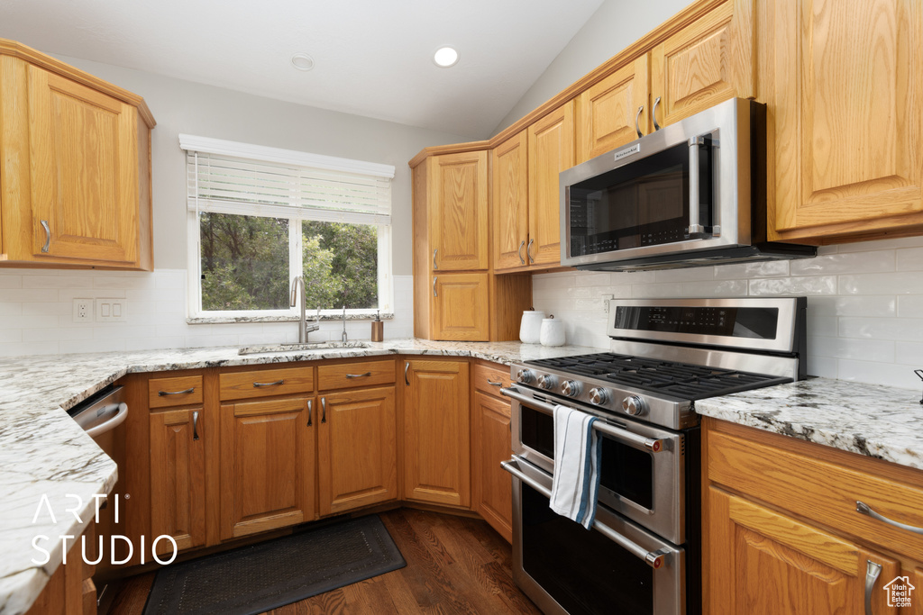 Kitchen with stainless steel appliances, light stone countertops, dark wood-style floors, lofted ceiling, and backsplash