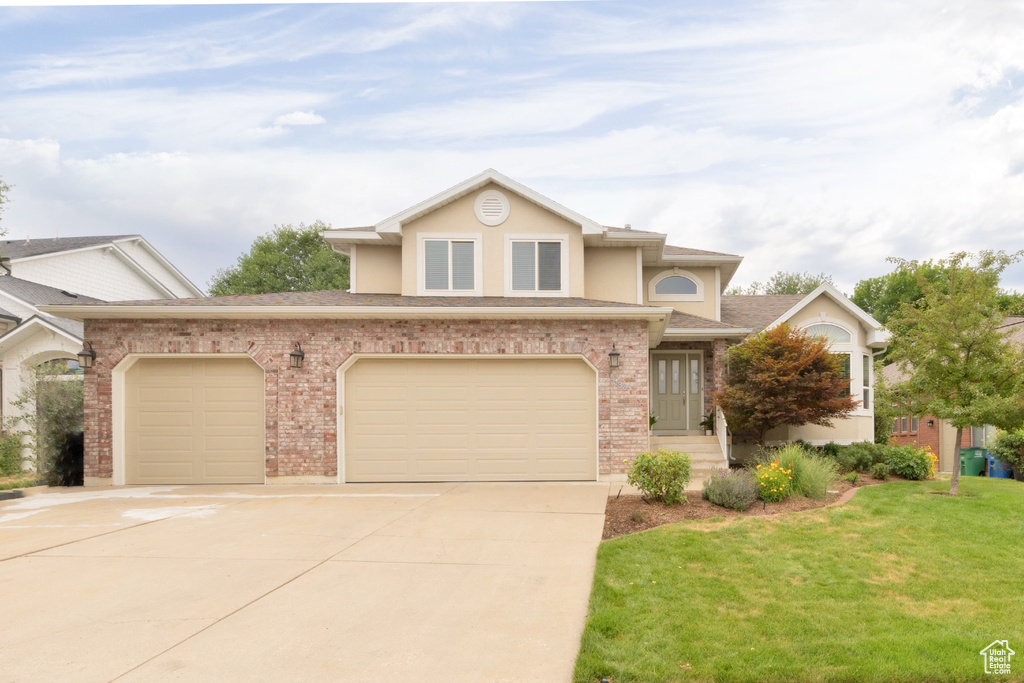View of front of property featuring driveway, roof with shingles, a front yard, brick siding, and stucco siding
