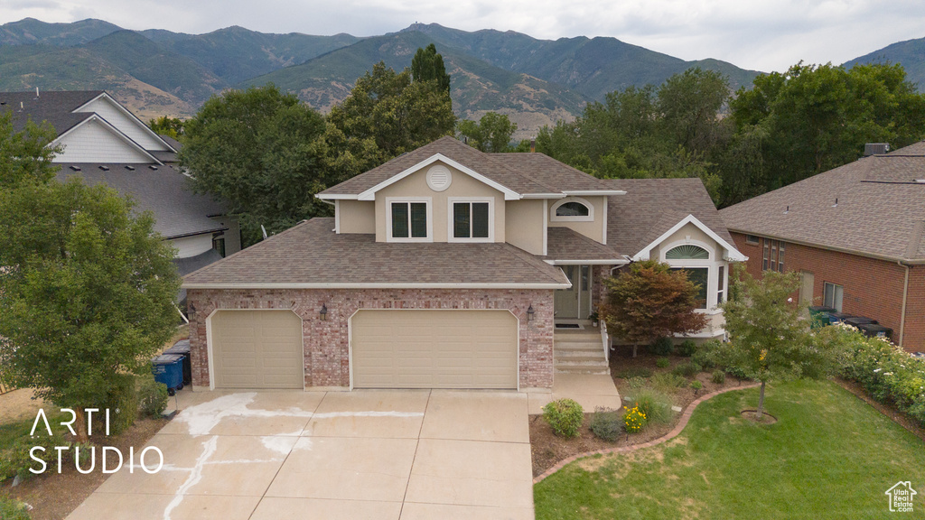 View of front of property featuring roof with shingles, concrete driveway, brick siding, a mountain view, and a front lawn