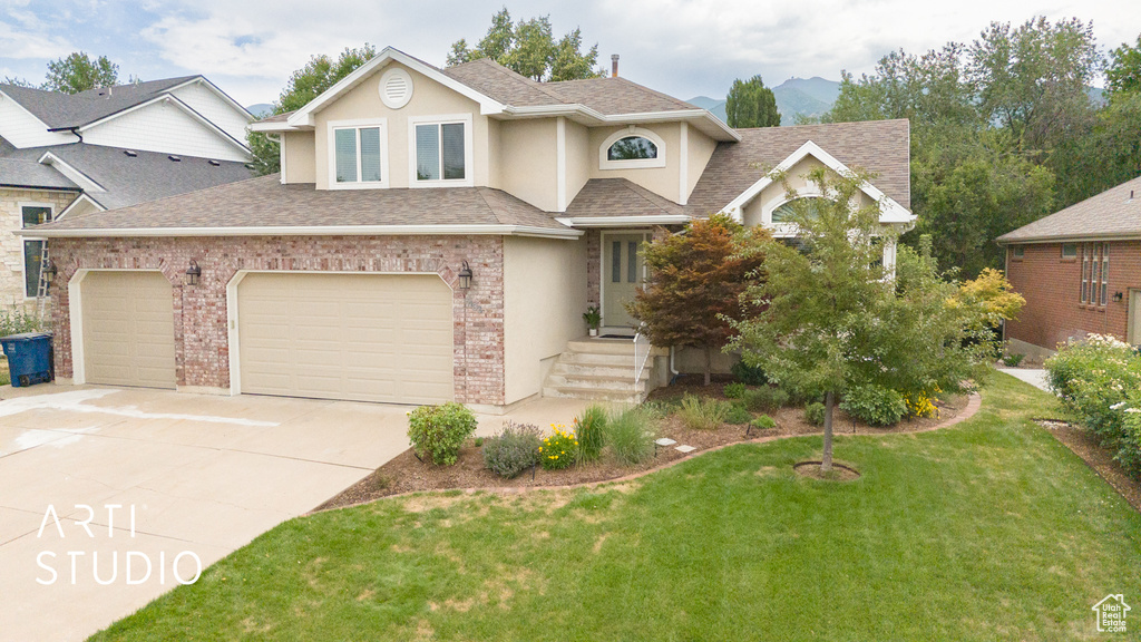 Traditional-style house featuring a shingled roof, concrete driveway, a front lawn, stucco siding, and a garage