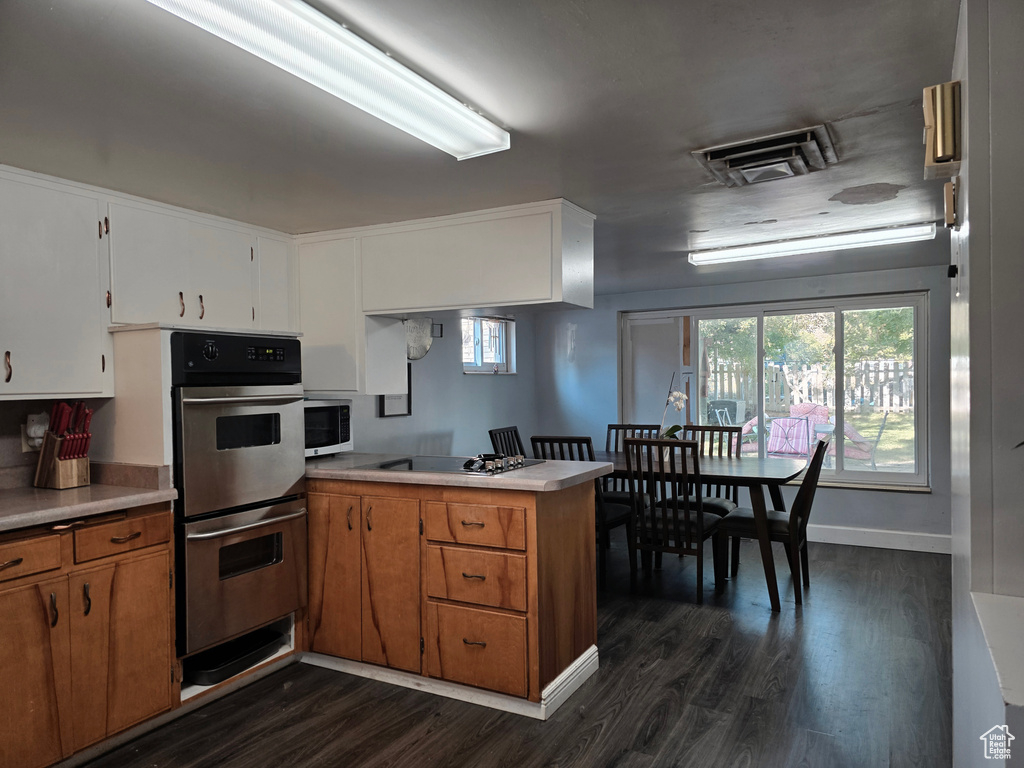 Kitchen with a peninsula, double oven, dark wood-style flooring, light countertops, and brown cabinetry