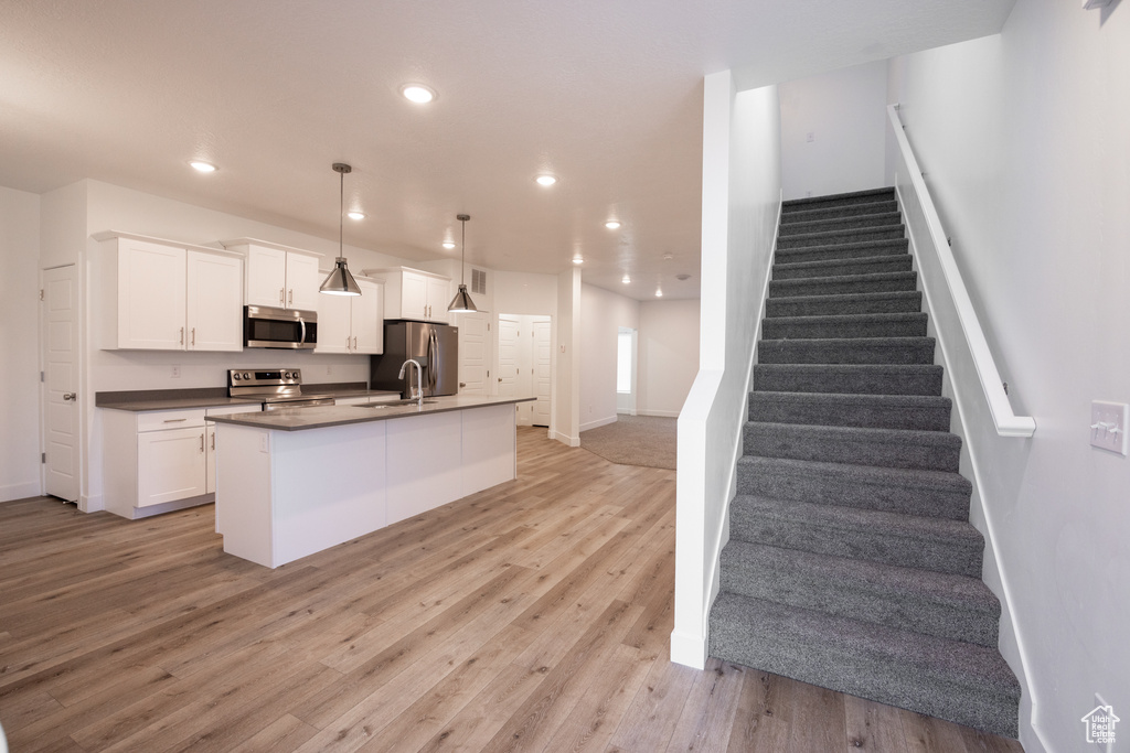 Kitchen featuring dark countertops, white cabinets, light wood-style flooring, stainless steel appliances, and a kitchen island with sink