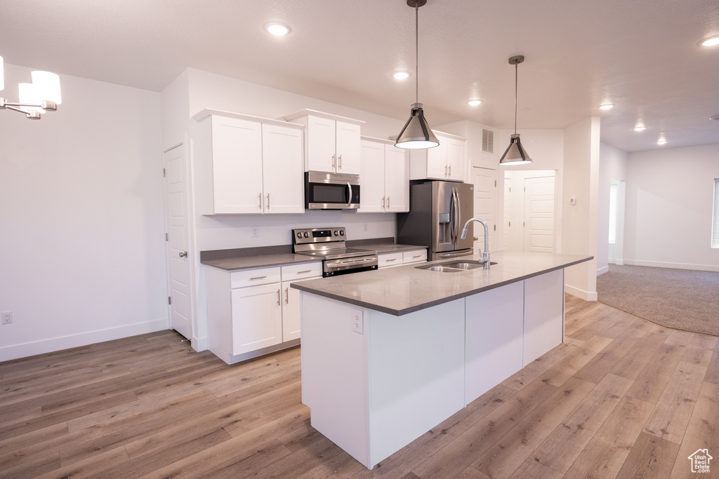 Kitchen with appliances with stainless steel finishes, an island with sink, white cabinetry, light wood finished floors, and recessed lighting