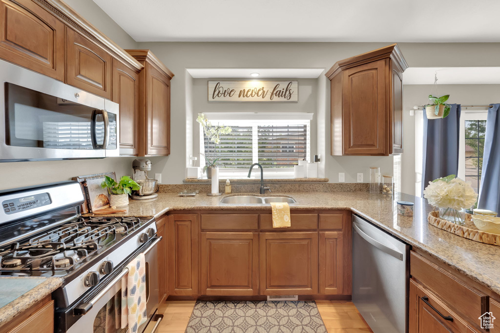 Kitchen featuring appliances with stainless steel finishes, light wood finished floors, brown cabinetry, and light stone countertops