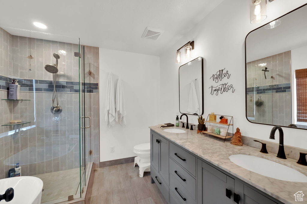 Bathroom featuring a shower stall, double vanity, wood finished floors, a soaking tub, and recessed lighting