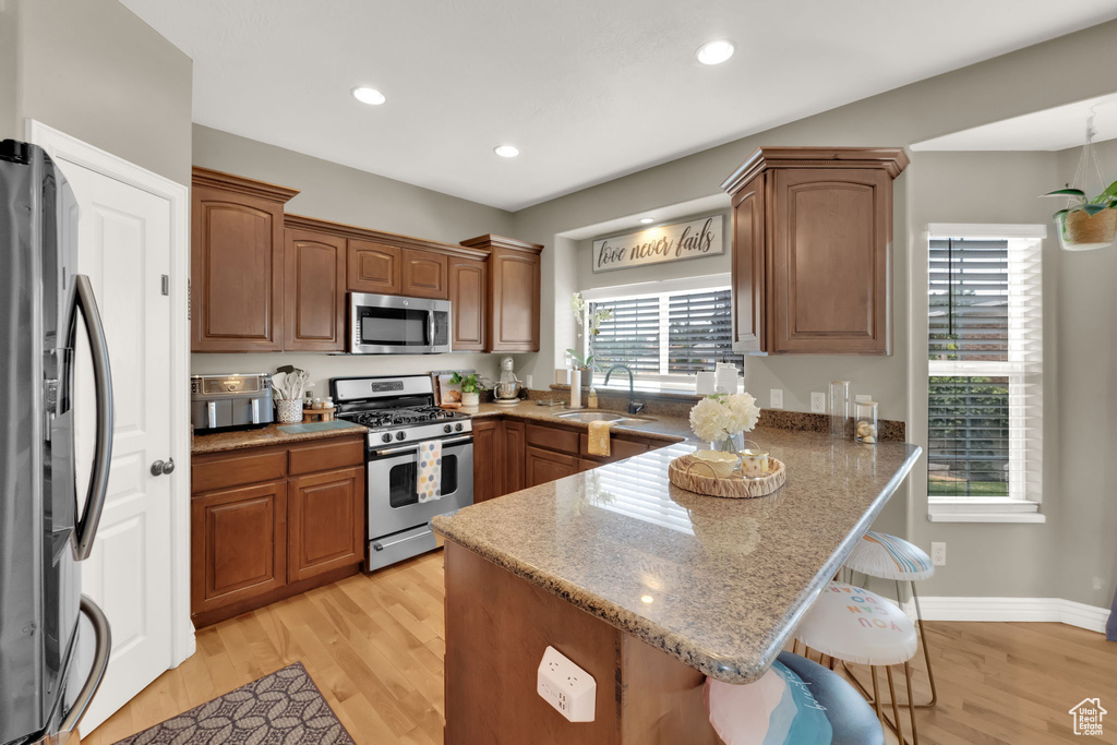 Kitchen with a peninsula, a kitchen bar, stainless steel appliances, light wood-type flooring, and recessed lighting
