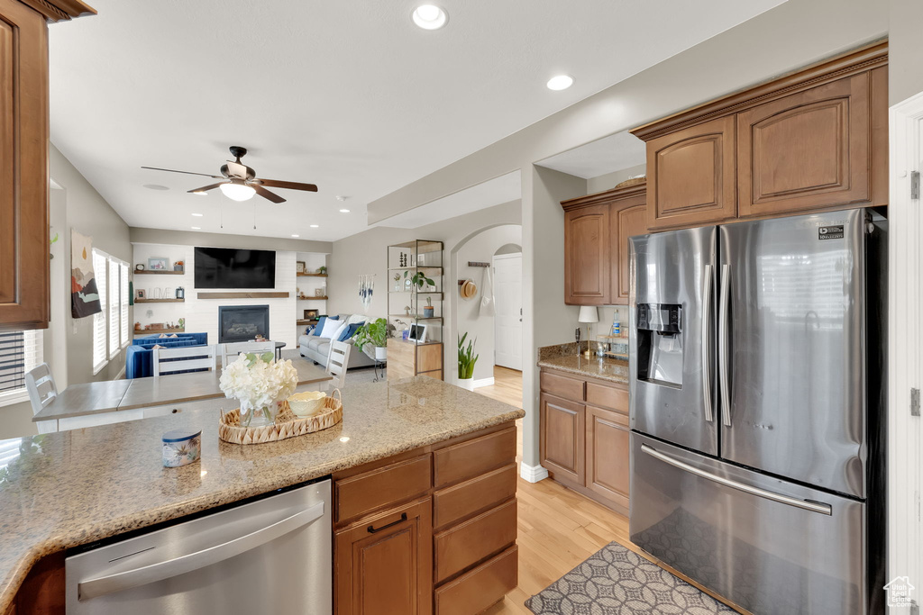 Kitchen featuring stainless steel appliances, ceiling fan, light wood-style flooring, a large fireplace, and light stone countertops