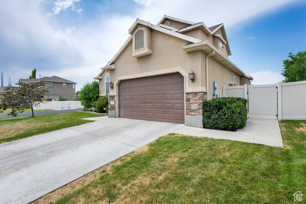 Traditional-style house featuring concrete driveway, stucco siding, stone siding, and a gate