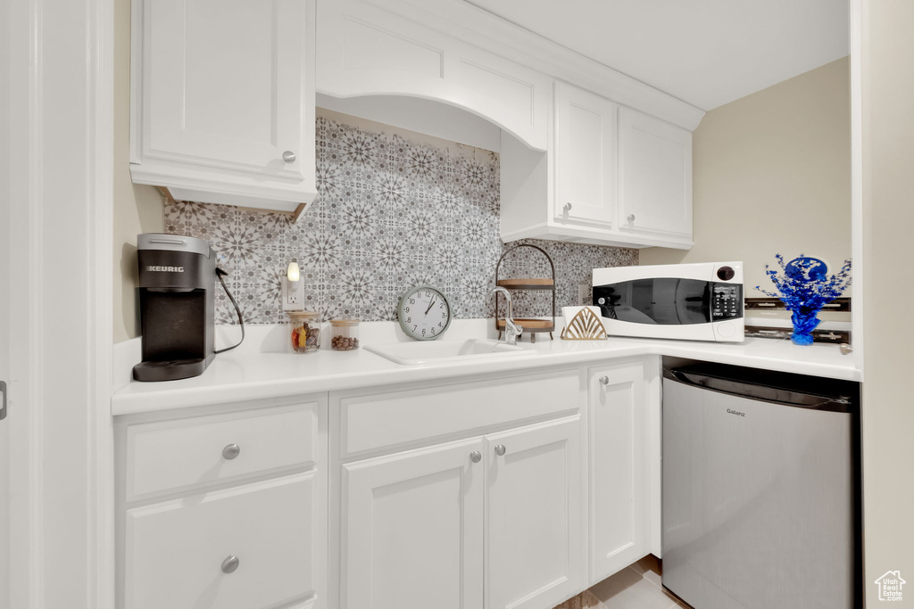 Kitchen featuring white microwave, decorative backsplash, white cabinets, light countertops, and dishwashing machine