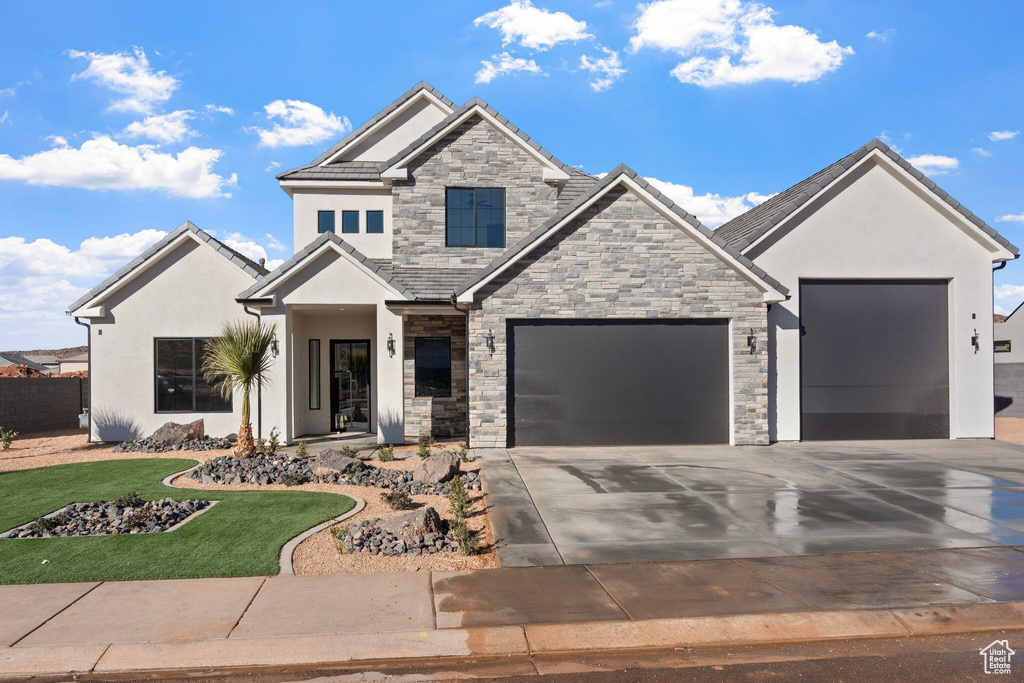View of front of house with stone siding, an attached garage, concrete driveway, and stucco siding