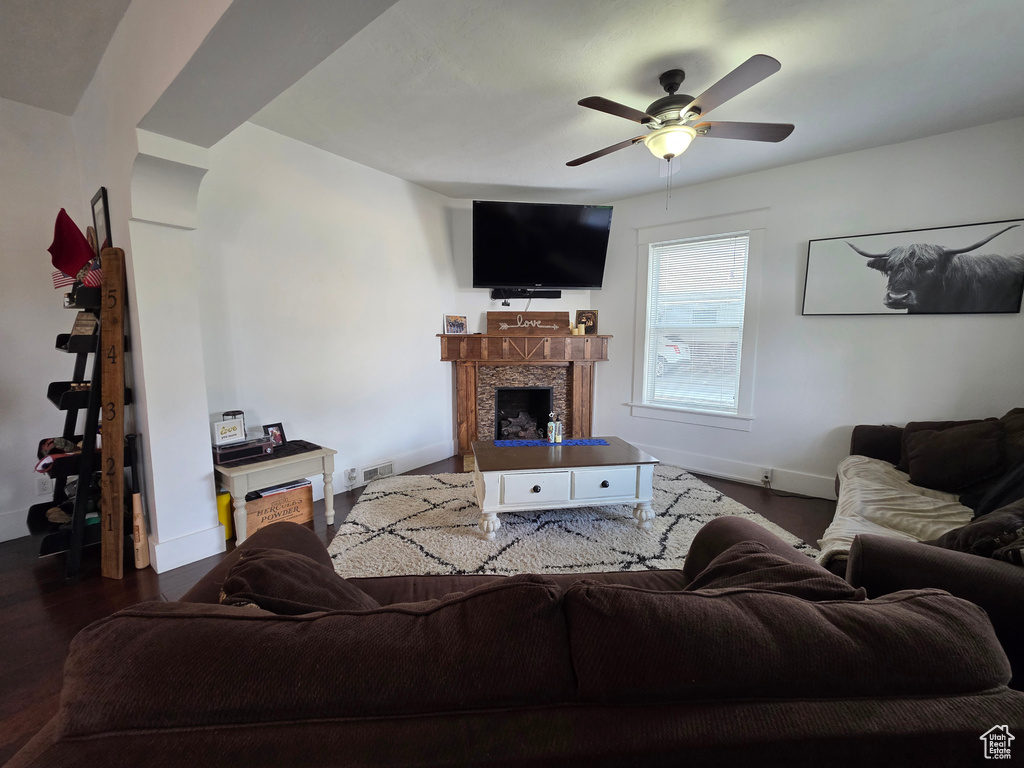 Living area with a fireplace, ceiling fan, and dark wood finished floors