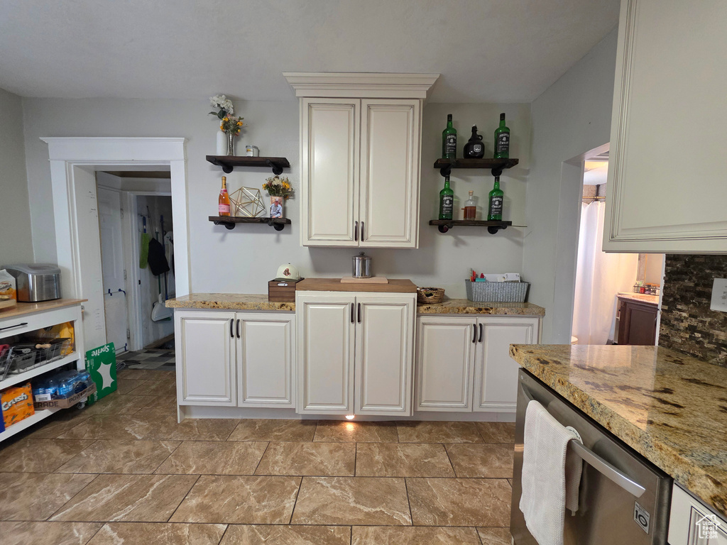 Kitchen featuring open shelves, dishwasher, and light stone counters