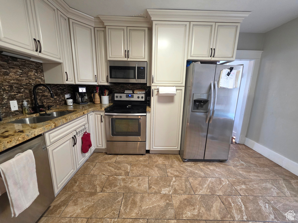 Kitchen featuring stainless steel appliances, tasteful backsplash, light stone countertops, and light stone finish floors
