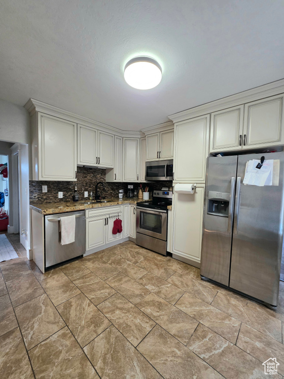 Kitchen with appliances with stainless steel finishes, tasteful backsplash, dark stone countertops, and light stone finish flooring