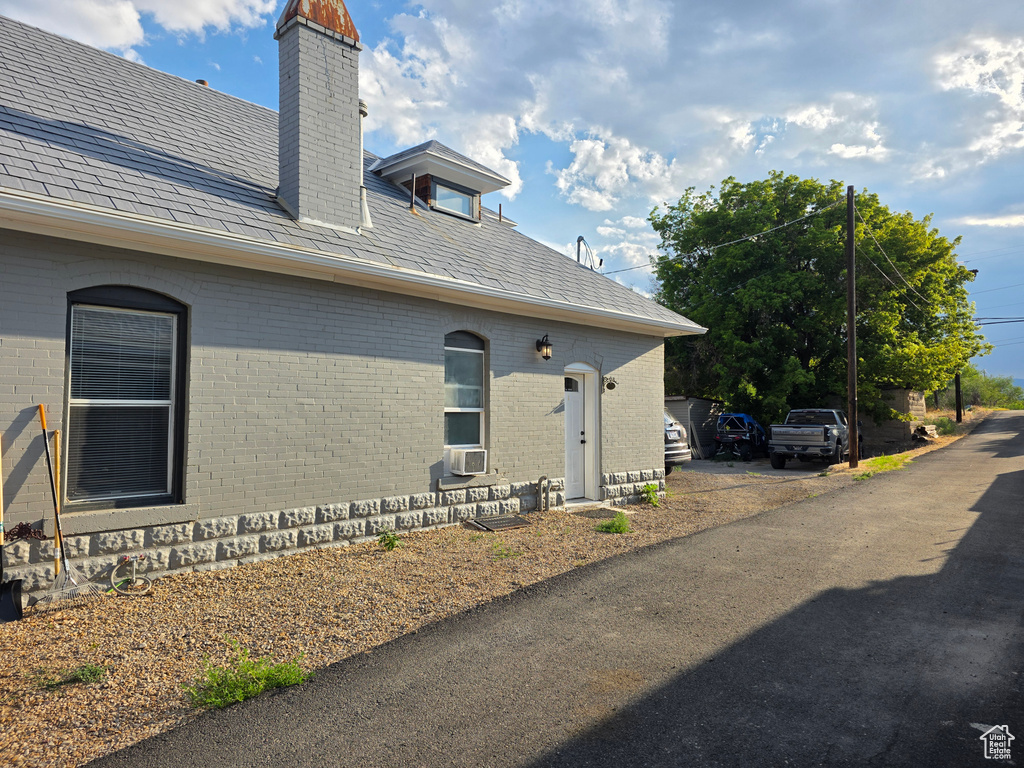 View of side of property with a chimney, brick siding, and a high end roof