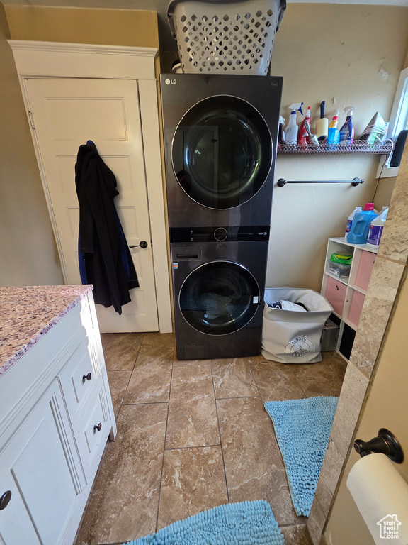 Laundry room with stacked washer / dryer, light stone finish flooring, and cabinet space