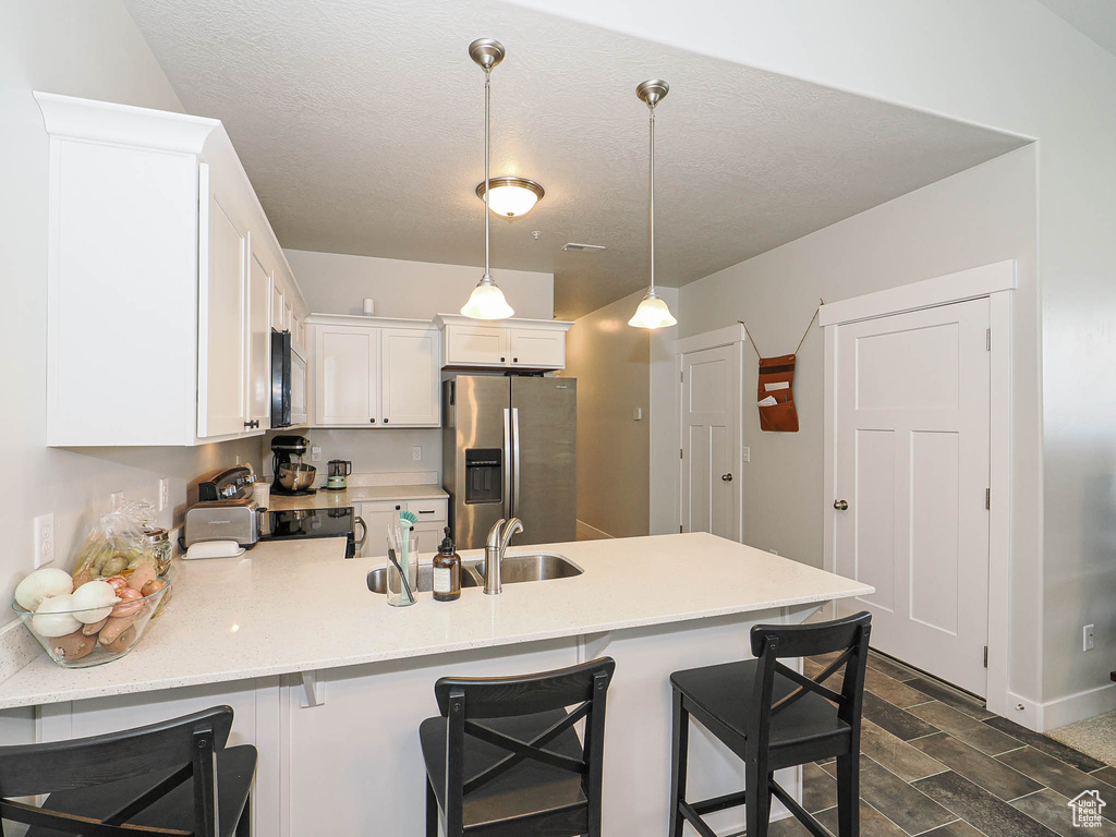 Kitchen featuring a peninsula, appliances with stainless steel finishes, white cabinetry, light countertops, and hanging light fixtures
