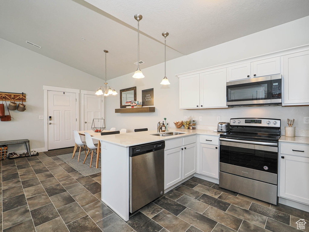 Kitchen with stainless steel appliances, lofted ceiling, a peninsula, white cabinetry, and a chandelier