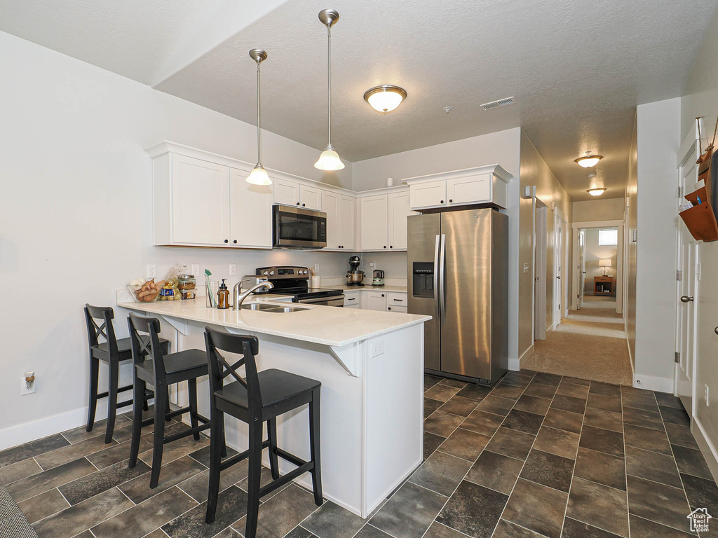 Kitchen featuring stainless steel appliances, a peninsula, light countertops, white cabinetry, and a breakfast bar area