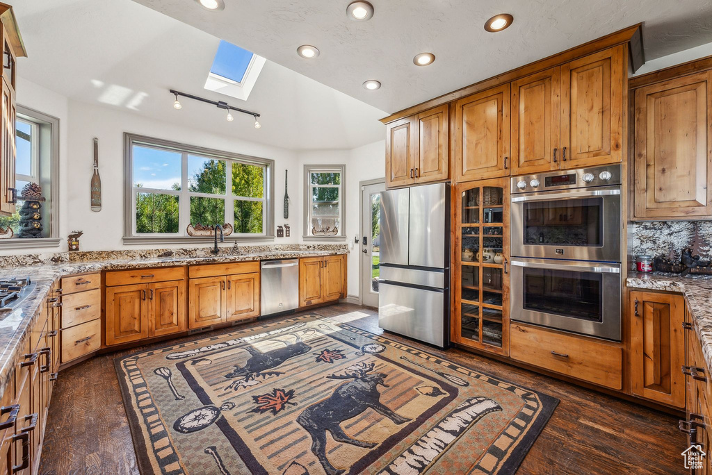 Kitchen featuring a skylight, appliances with stainless steel finishes, recessed lighting, light stone counters, and dark wood-type flooring