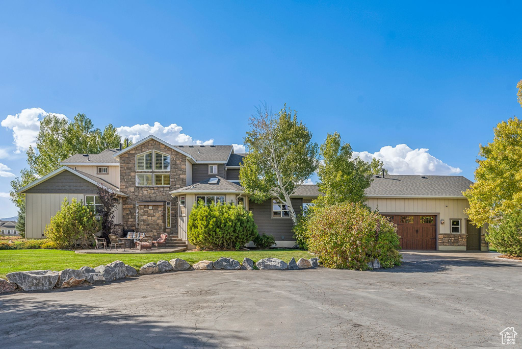 View of front of home featuring stone siding, a shingled roof, a front lawn, and a garage