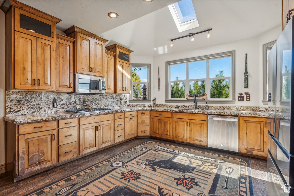 Kitchen with a skylight, healthy amount of natural light, appliances with stainless steel finishes, light stone counters, and recessed lighting