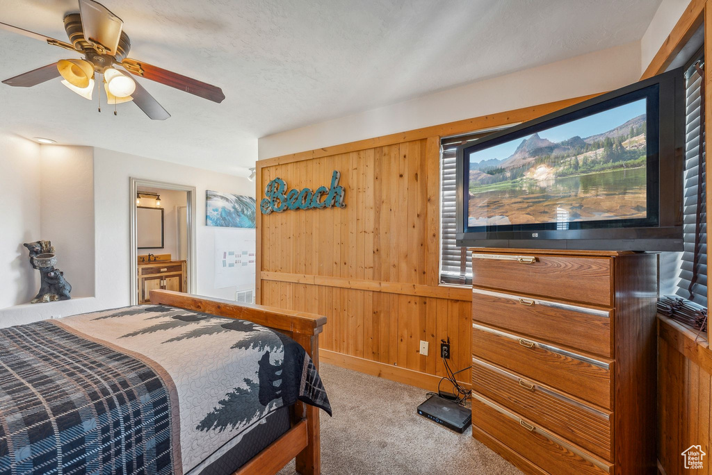 Bedroom with carpet floors, wooden walls, ensuite bath, and ceiling fan