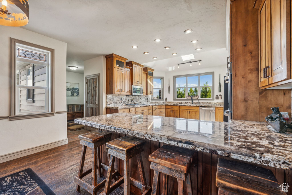 Kitchen with a peninsula, dark wood-style floors, recessed lighting, a breakfast bar area, and brown cabinetry