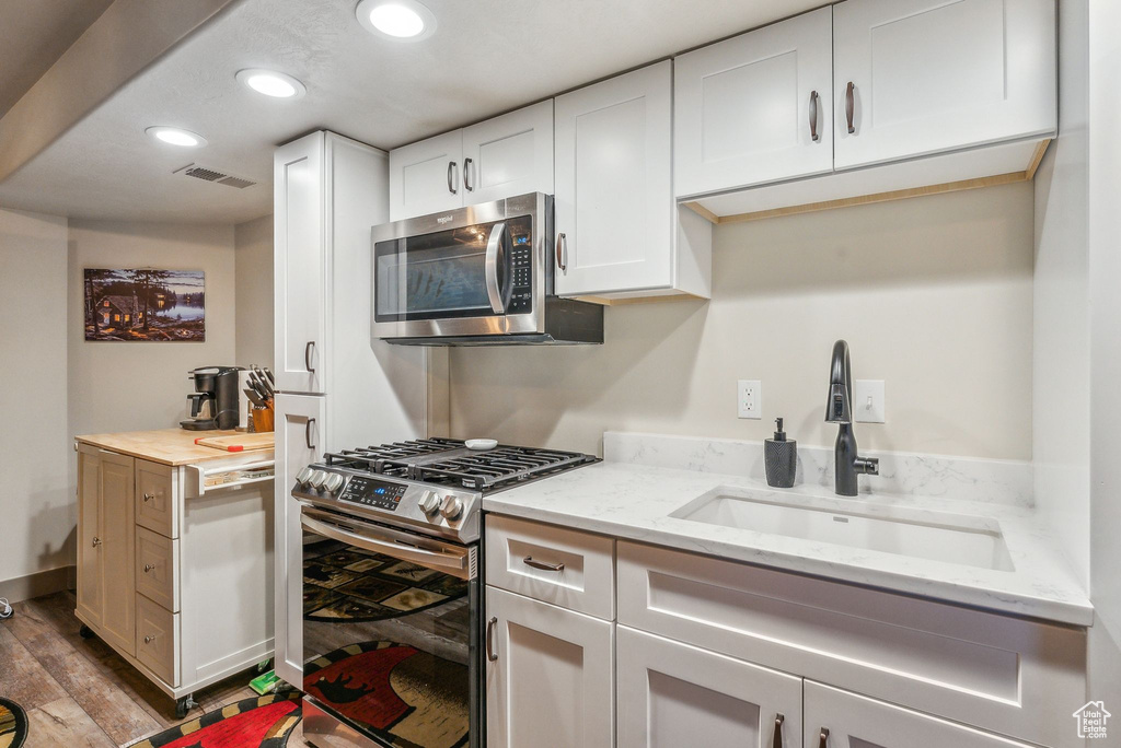 Kitchen with appliances with stainless steel finishes, recessed lighting, white cabinetry, light stone countertops, and wood finished floors