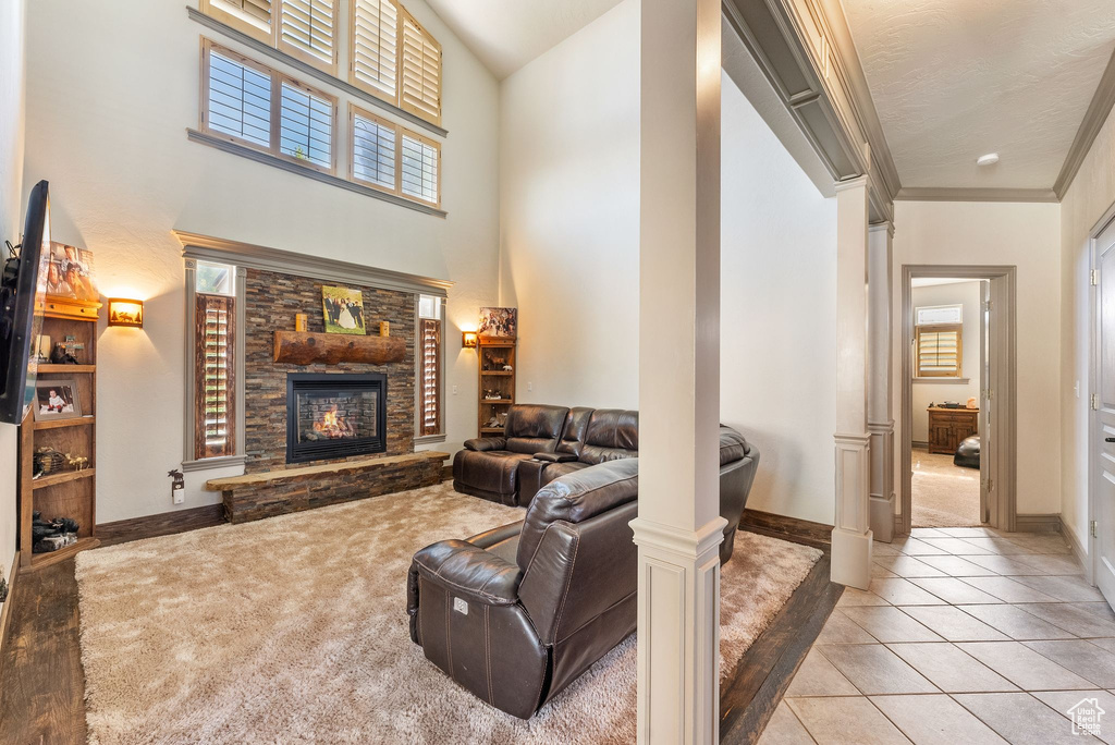Living room with a stone fireplace, light carpet, a high ceiling, light tile patterned floors, and crown molding