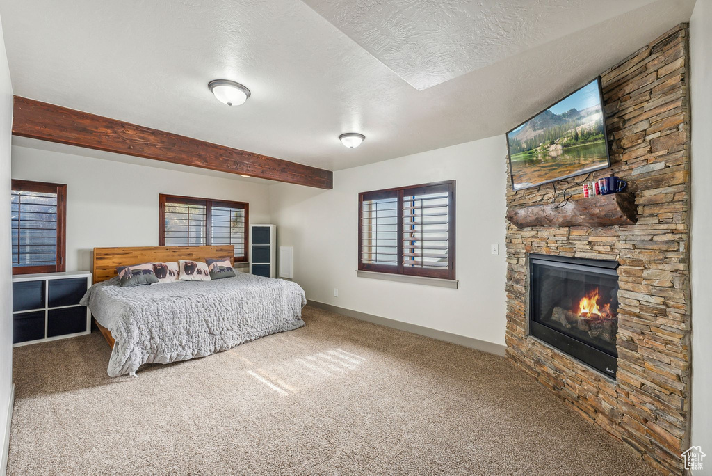Carpeted bedroom with a fireplace, a textured ceiling, and beam ceiling