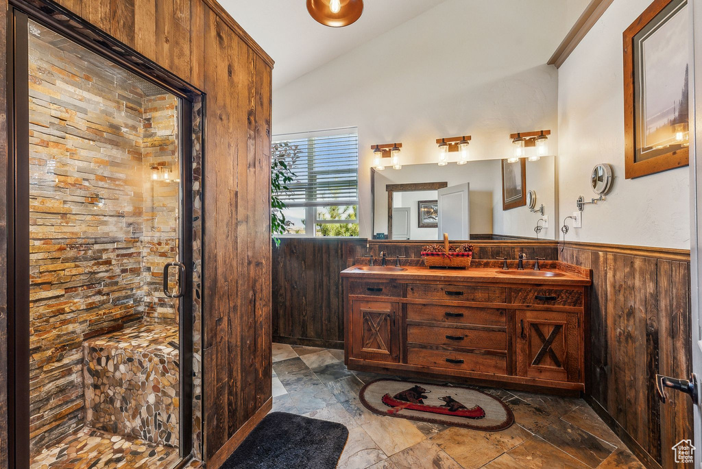 Bathroom featuring lofted ceiling, double vanity, a stall shower, wainscoting, and wooden walls