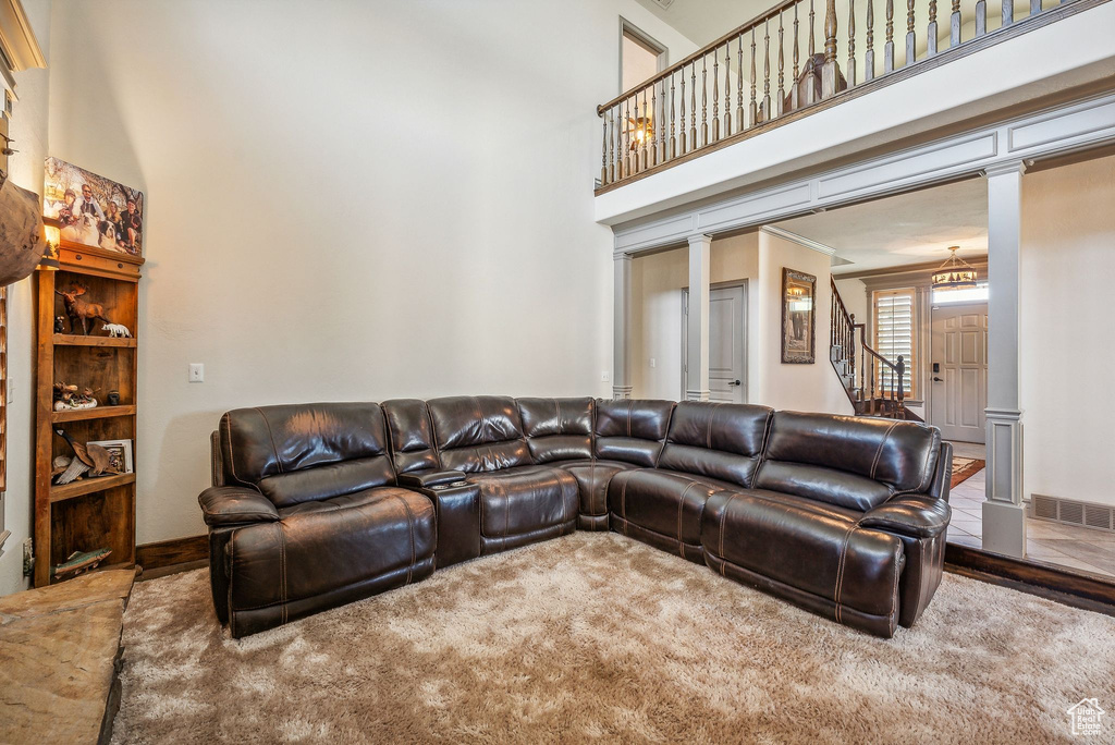 Carpeted living area featuring ornate columns, stairs, a high ceiling, and crown molding