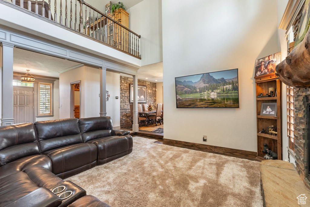 Carpeted living room with a fireplace with raised hearth, a high ceiling, ornate columns, and crown molding