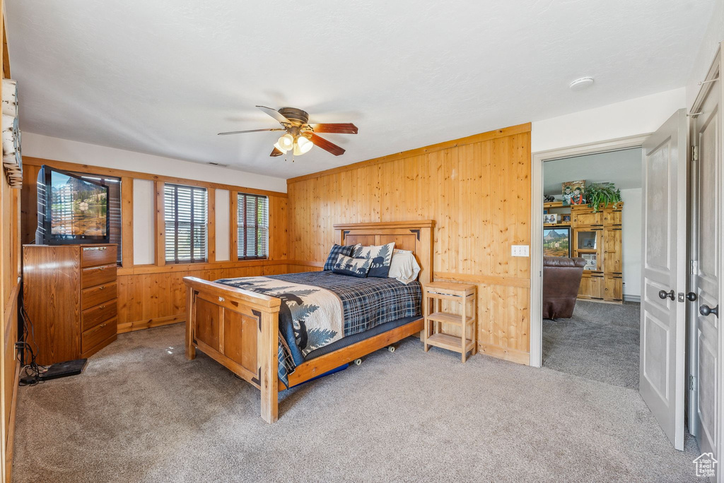 Bedroom featuring carpet flooring, wood walls, and ceiling fan