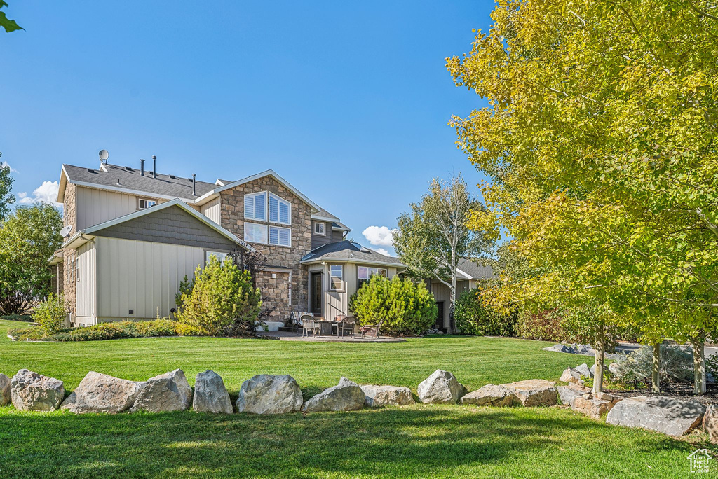 Rear view of property featuring a yard, a patio area, and stone siding
