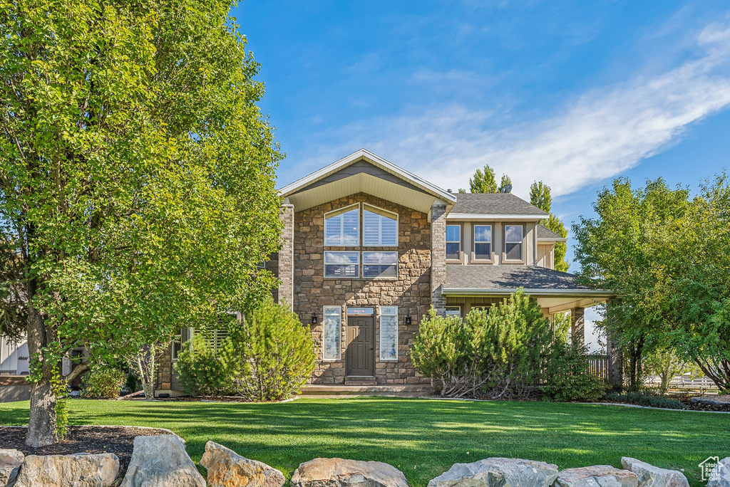 View of front of home with a front yard, stone siding, and roof with shingles