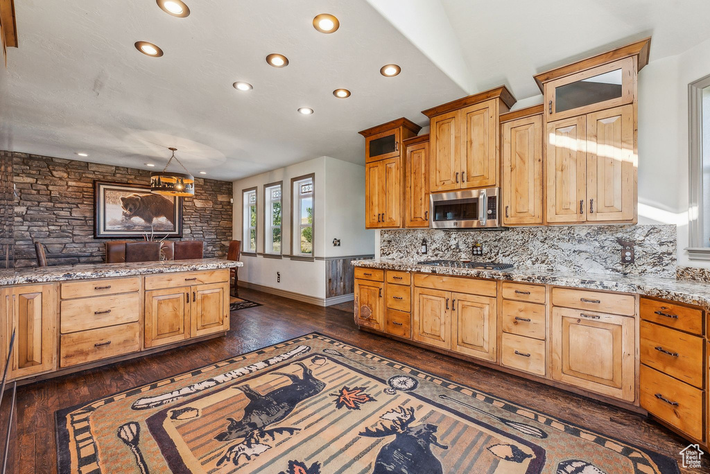 Kitchen featuring recessed lighting, dark wood-type flooring, decorative backsplash, light stone countertops, and stainless steel appliances