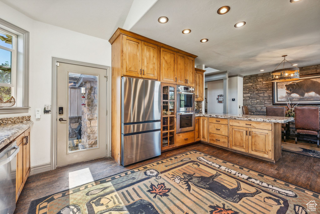 Kitchen featuring appliances with stainless steel finishes, recessed lighting, a peninsula, dark wood-style floors, and light stone countertops