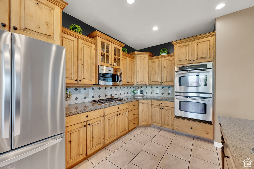 Kitchen featuring appliances with stainless steel finishes, backsplash, glass insert cabinets, light brown cabinets, and recessed lighting