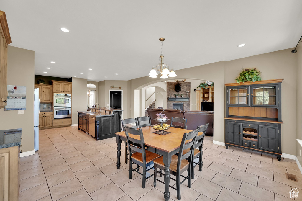 Dining room featuring arched walkways, light tile patterned floors, recessed lighting, a chandelier, and a stone fireplace