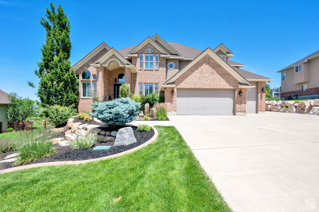 View of front facade featuring a garage, brick siding, concrete driveway, and a front yard