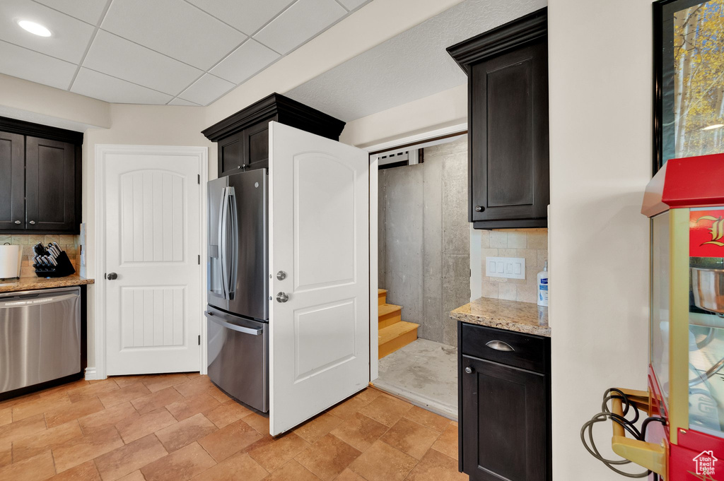 Kitchen featuring stainless steel appliances, tasteful backsplash, light stone countertops, dark cabinets, and stone finish floors