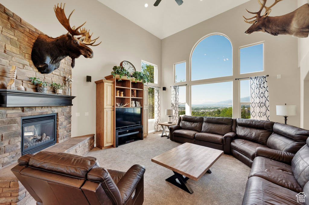 Living room with high vaulted ceiling, light colored carpet, a ceiling fan, and a stone fireplace