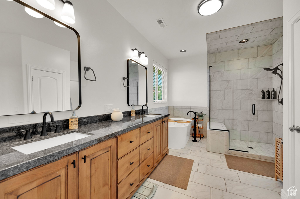 Full bath with a shower stall, a freestanding bath, double vanity, marble look tiles, and recessed lighting