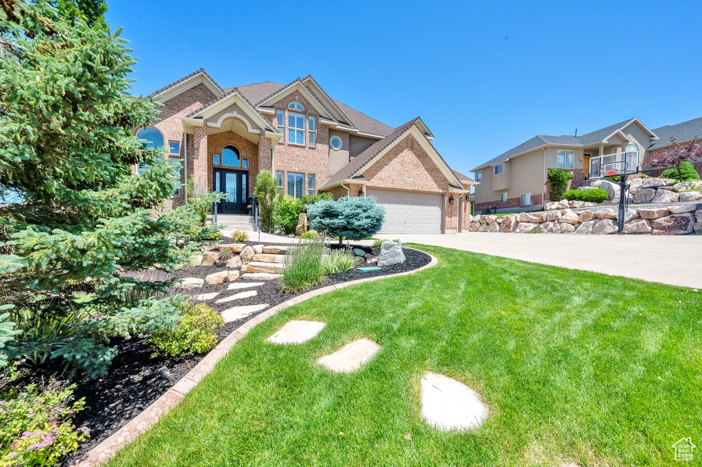 View of front of home featuring brick siding, a garage, driveway, and a front yard