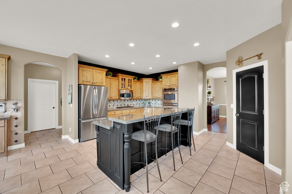 Kitchen with stainless steel appliances, arched walkways, light tile patterned floors, a kitchen breakfast bar, and recessed lighting